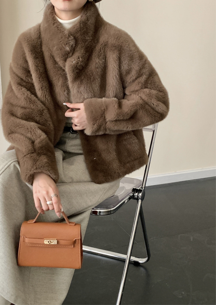 lily Mila plush mink fur coat in brown with a stand collar, worn over a white top and beige trousers while seated.