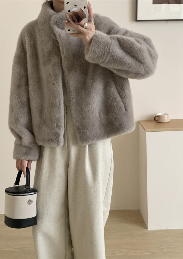 lily Mila plush mink fur coat in grey with a stand collar, styled with cream trousers and a small cylindrical bag.