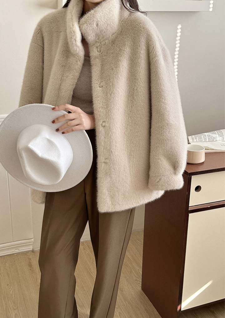 lily Mila plush mink fur coat in beige with a stand collar, worn with brown trousers and holding a white hat.